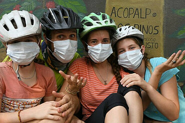 Seba, Alberta, Angela und Anna tragen Fahrradhelm und Mund-Nasen-Schutz. 